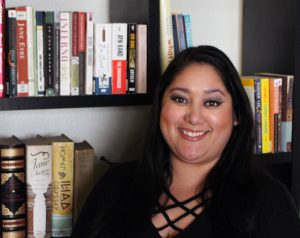 Christina Villa headshot; hispanic woman with black shirt in front of a bookshelf.
