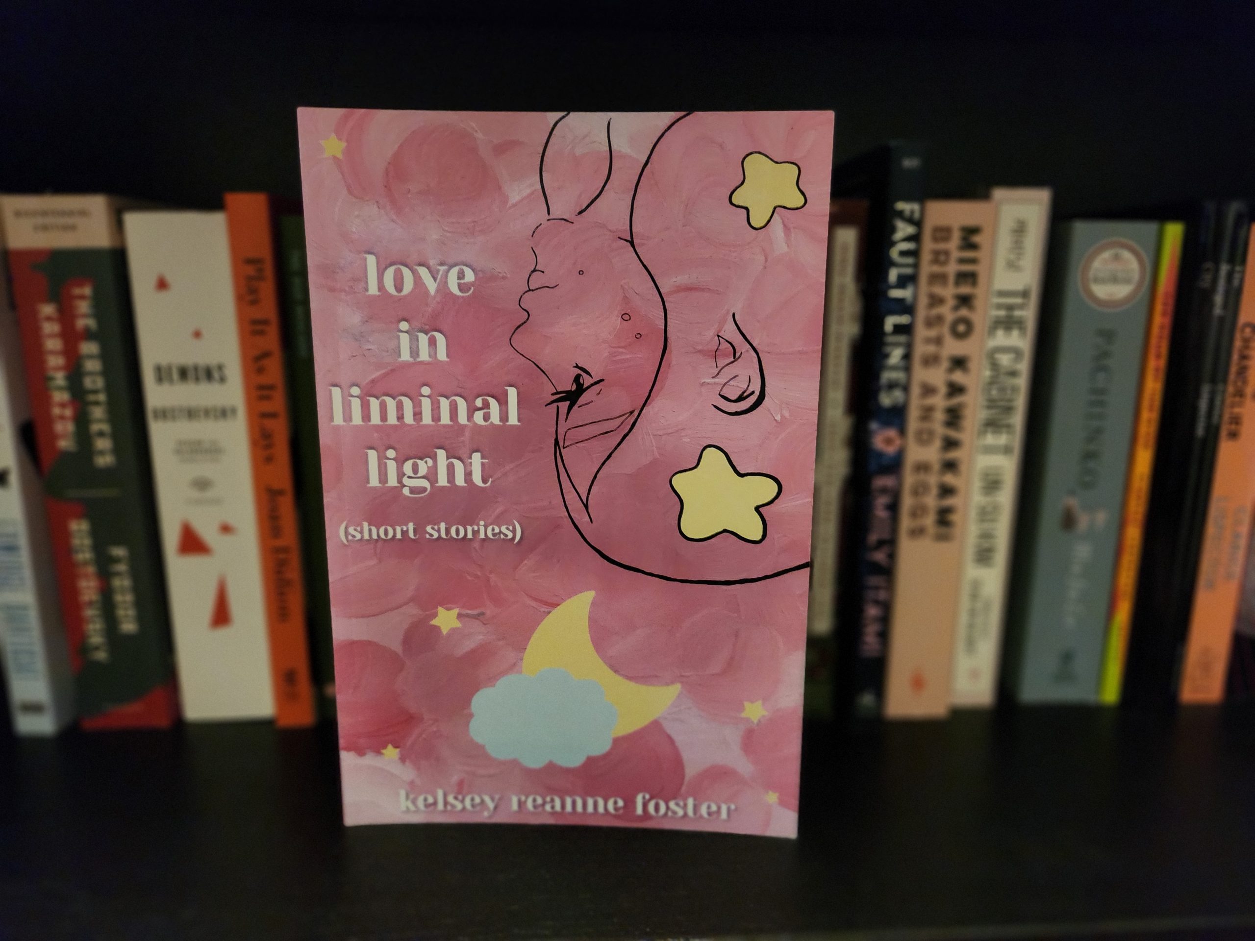 A pink book placed on a book shelf that reads: love in liminal light.